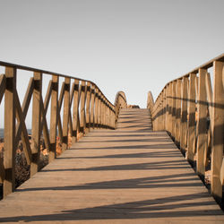 Empty long wooden bridge against clear sky