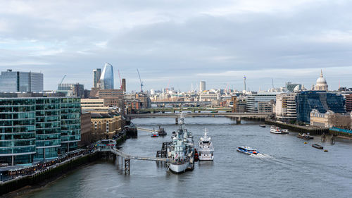 Boats in river by buildings in city against sky