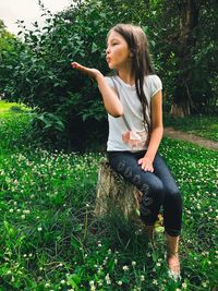 Girl blowing kiss while sitting on tree stump at park