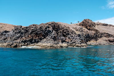 Scenic view of rock formation in sea against blue sky
