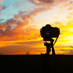 Tripod camera on silhouette field against sky during sunset
