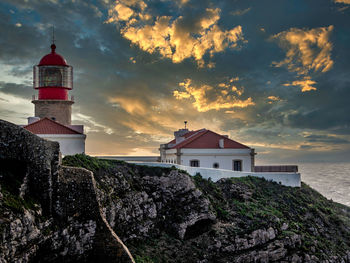 Lighthouse by sea and buildings against sky