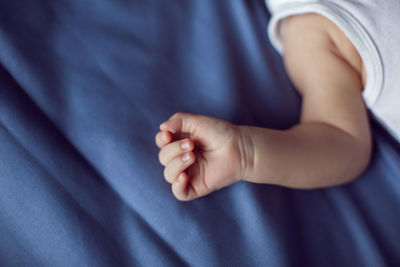 Close up hand baby boy blonde in white bodysuit lying on the bed