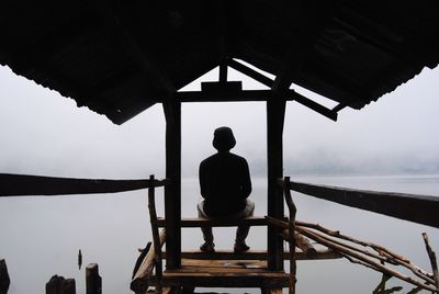 Rear view of man sitting on pier against sky