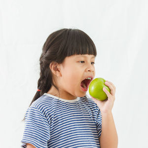 Portrait of boy eating apple against white background