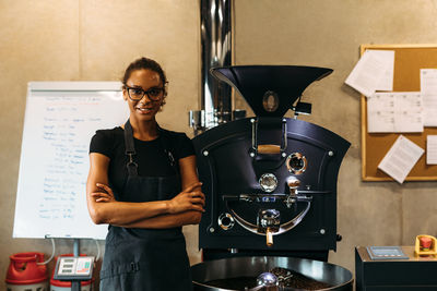 Portrait of female owner standing by coffee grinder in cafe