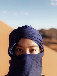 Portrait of woman with covered face on desert against sky
