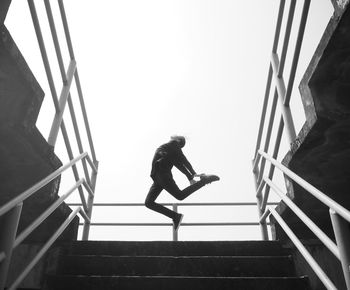 Low angle view of person jumping by staircase against clear sky