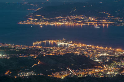 Aerial view of illuminated city by sea against sky at night