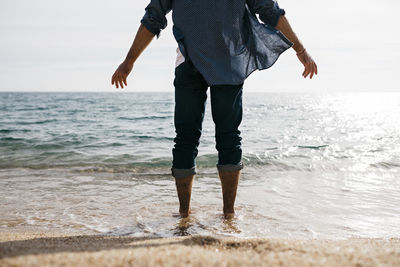 Mature man standing in water's edge against clear sky at beach