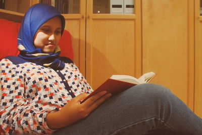 Young woman reading book while sitting at home