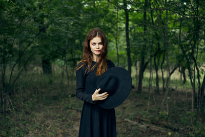 Portrait of young woman standing against trees