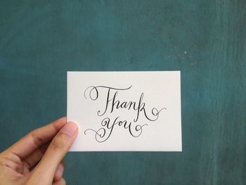 Close-up of hand holding paper with thank you text against wall