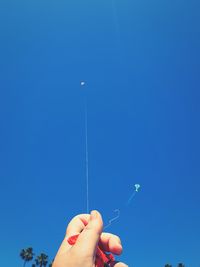 Low angle view of person hand against clear blue sky