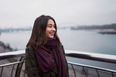 Beautiful calm young woman staying near river with closed eyes and expressing delight.