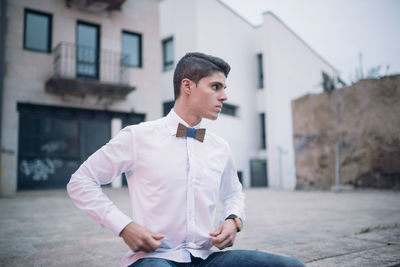 Young man looking away while sitting in city