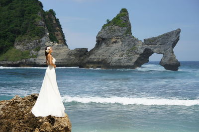 Side view of bride standing on rock by sea