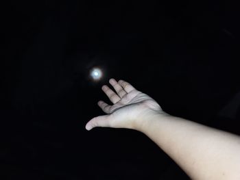 Close-up of person hand against moon over black background