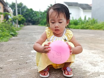 Cute girl holding balloon while crouching on street