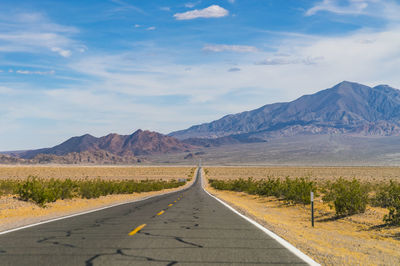 Empty road leading towards mountains against sky