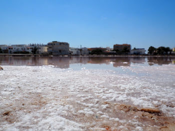 View of frozen river in front of canal against clear blue sky