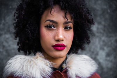 Fashionable young woman with curly hair against wall