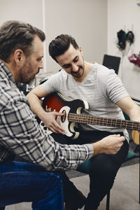 Mature man teaching student guitar while sitting in classroom