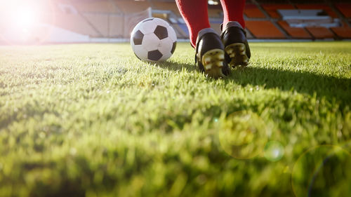 Low section of man playing soccer at stadium on sunny day