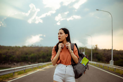 Young woman looking away while standing on road against sky