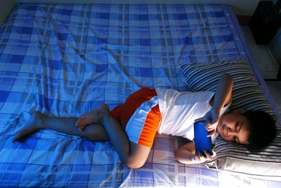 High angle view of boy using smart phone while lying down on bed at home