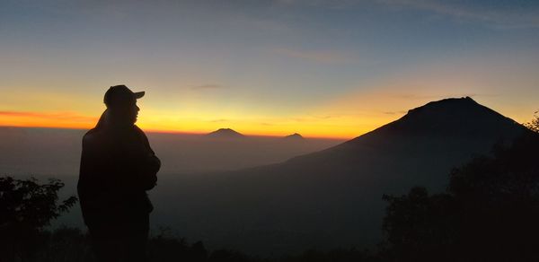 Silhouette man looking at mountains against sky during sunset