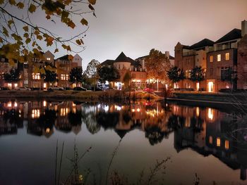 Illuminated buildings by lake against sky at night