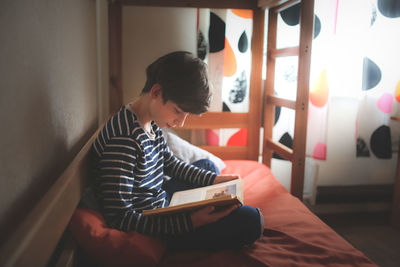 Teenager reads a book on a bed in his room, darkness, a real interior.