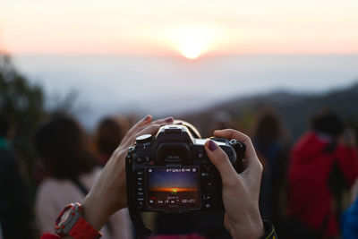 Cropped hands of woman photographing with camera during sunset