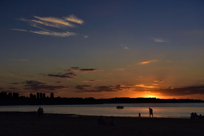 Silhouette people on beach against sky during sunset