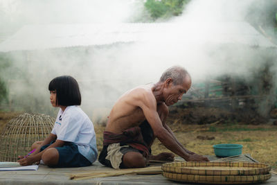 Senior man making wicker basket while granddaughter studying on table