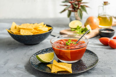 Tomato dip with nachos tortilla in bowl and basic ingredients aside