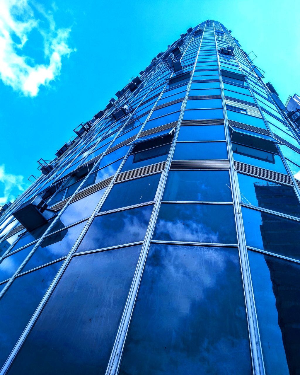 LOW ANGLE VIEW OF GLASS BUILDING AGAINST BLUE SKY