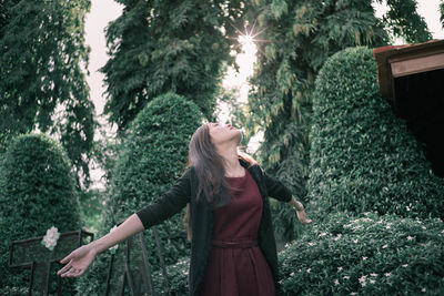 Young woman standing with arms outstretched against plants at park