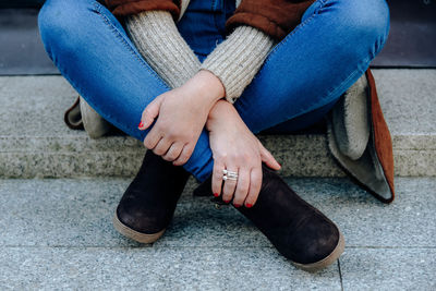 Low section of woman holding legs while sitting on footpath