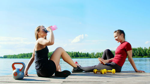 Two beautiful, athletic blonde girls, women have rest after training outdoors, drink water, talk