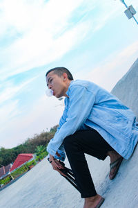 Side view of young man looking at camera against sky