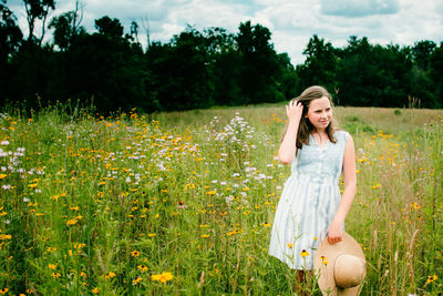 Young woman holding a sun hat in meadow.