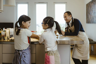Siblings baking with each other while father standing in kitchen at home