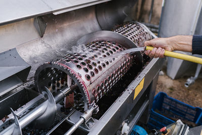 Hand of worker washing crushing machinery from hose at winery