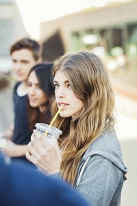 Female student drinking juice while standing with friends in city