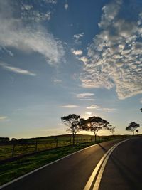 Empty road by trees on field against sky