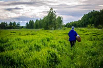 Rear view of woman walking on field against sky