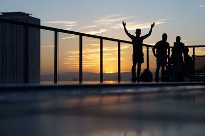 Silhouette people standing by sea against sky during sunset