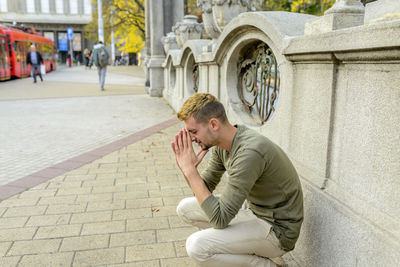 Side view of thoughtful young man crouching on footpath